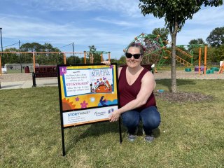 Miss Elizabeth smiles by the title sign for the Maybe Something Beautiful StoryWalk.